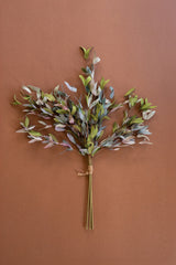 A dried artificial eucalyptus branch bundle with muted green, gray, and soft pink leaves tied with natural twine, displayed against a solid terracotta brown background.