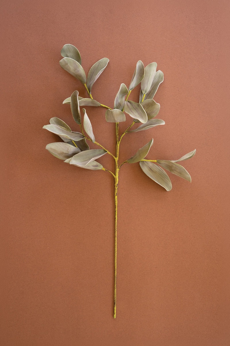 A single artificial eucalyptus branch with muted sage-green leaves and a yellow stem, displayed against a solid terracotta background.