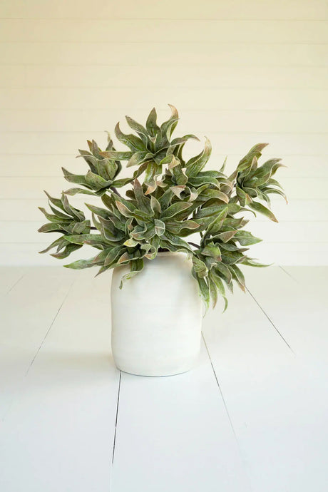 Artificial green potted plant on a white floor with a white wall background