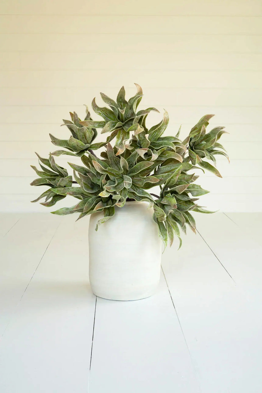 Artificial green potted plant on a white floor with a white wall background