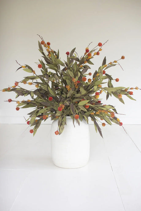A dried floral arrangement featuring olive green leaves and clusters of small orange-red berries, presented in a matte white ceramic vase against a clean white background.
