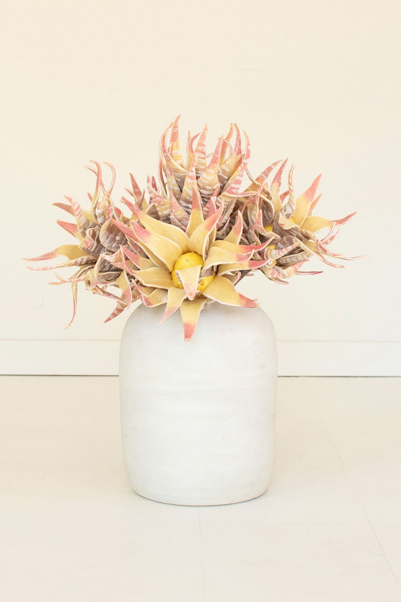A decorative succulent arrangement with pale yellow and pink variegated leaves, displayed in a matte white ceramic vase against a clean off-white background.