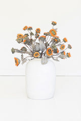 A white ceramic vase filled with dried orange and yellow flowers, set against a clean white background.