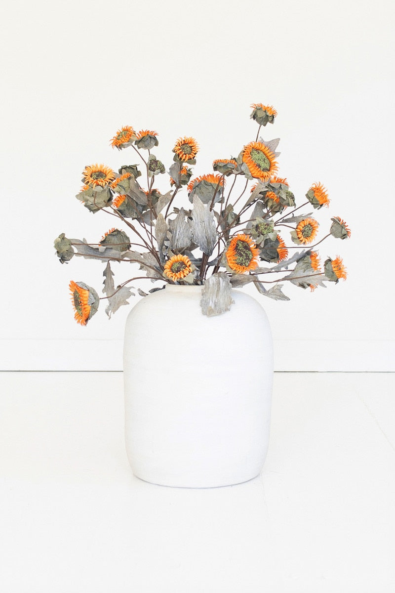 A white ceramic vase filled with dried orange and yellow flowers, set against a clean white background.