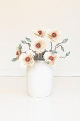 faux floral stem showcases softly layered blooms accented with warm yellow centers and muted greenery for a naturally weathered garden-inspired look in a white vase
