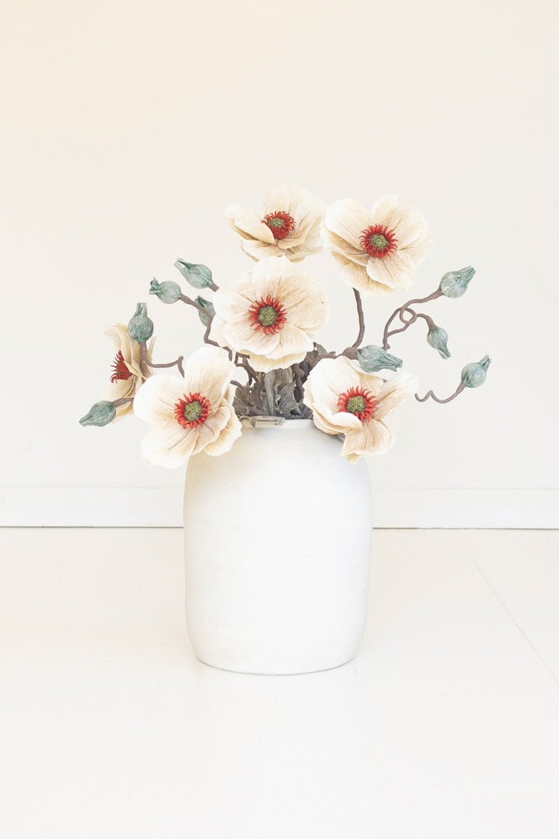 faux floral stem showcases softly layered blooms accented with warm yellow centers and muted greenery for a naturally weathered garden-inspired look in a white vase
