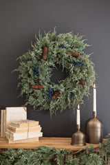 Faux evergreen wreath with dark blue berries and pine cones hung above a shelf