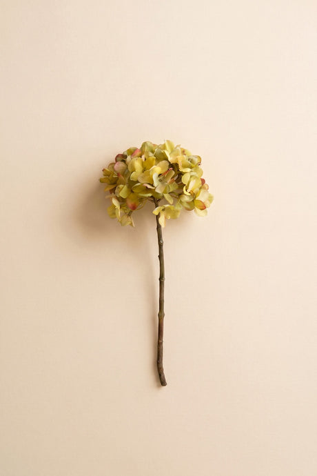 A single artificial flower stem with a round cluster of pale yellow-green hydrangea-like blooms on a thin brown stem, centered against a plain warm beige background.