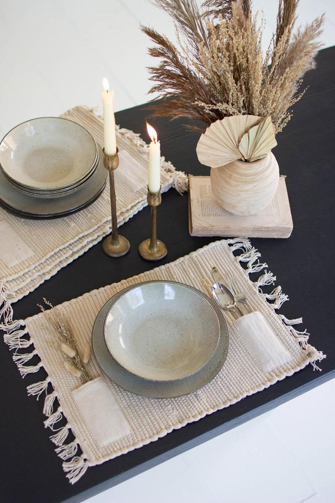 ceramic plate and bowl in oatmeal color on top of each other on placemats with silverware and burning candles