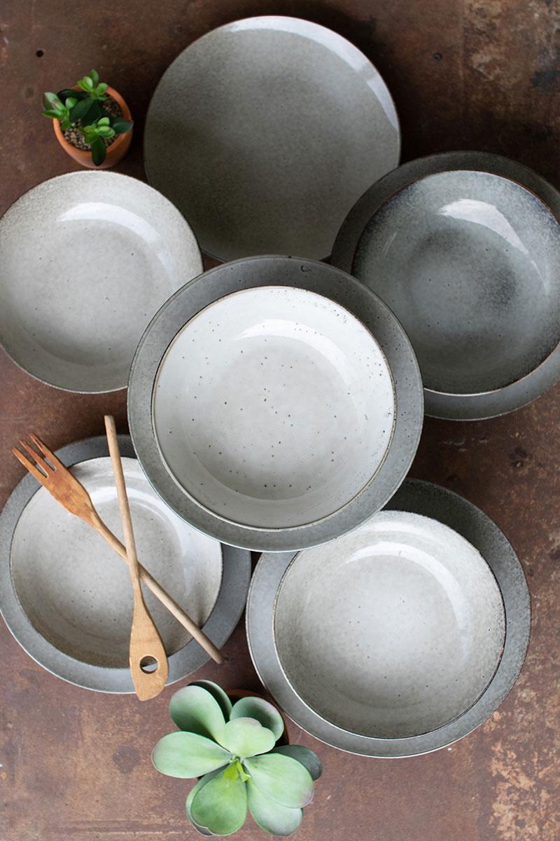 several pairs of ceramic plates and bowls in oatmeal color on top of each other - top down view