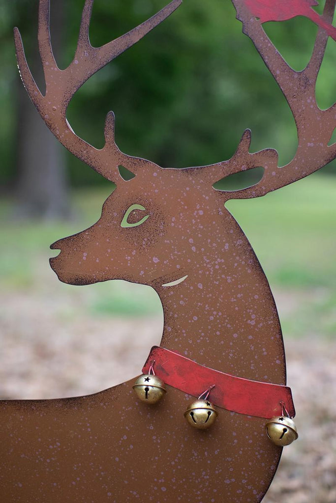 close-up of head of male deer, its antlers and red ribbon around its neck holding 3 bells