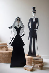 Skeleton couple in formal attire standing on stacked books against a plain background