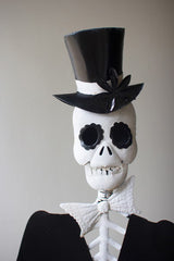 Skeleton wearing a black top hat and bow tie against a plain background
