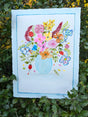 Original watercolor painting depicting a translucent blue glass vase holding a myriad of colorful flower bouquet.