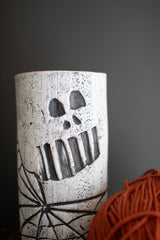 Clay wine holder with skull face and spider web design against a dark background