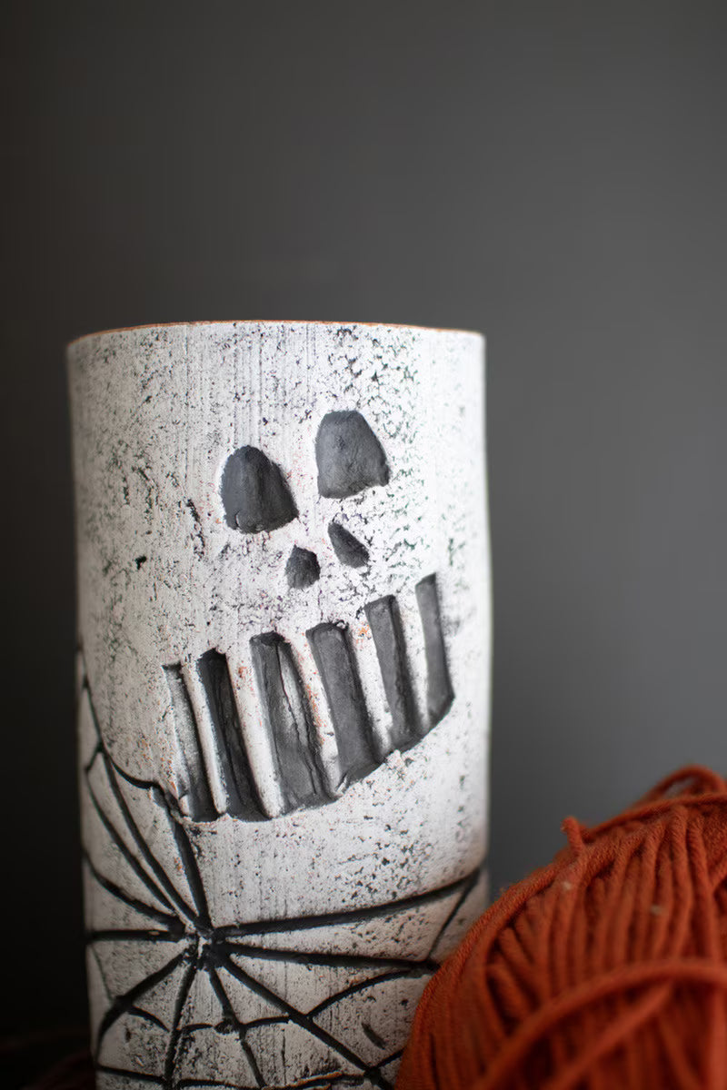 Clay wine holder with skull face and spider web design against a dark background