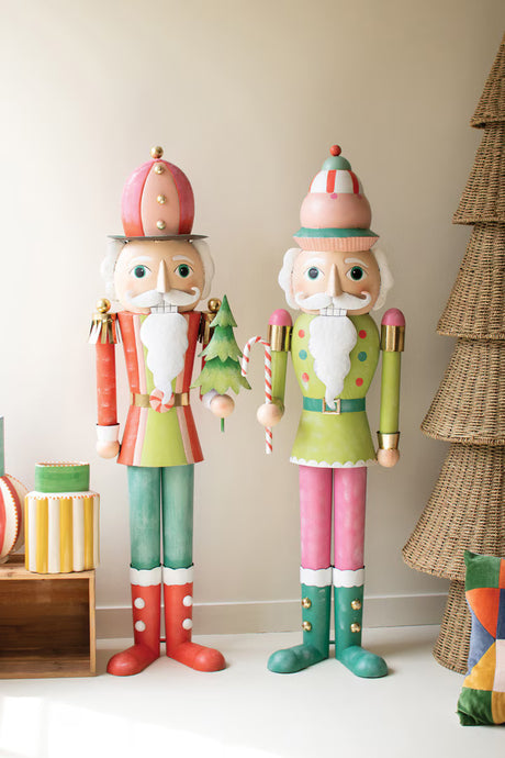 Two pastel colored nutcrackers standing next to a Christmas tree and gift box
