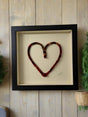 dark red color mix fabric heart in black frame behind museum glass hung on wood slab wall