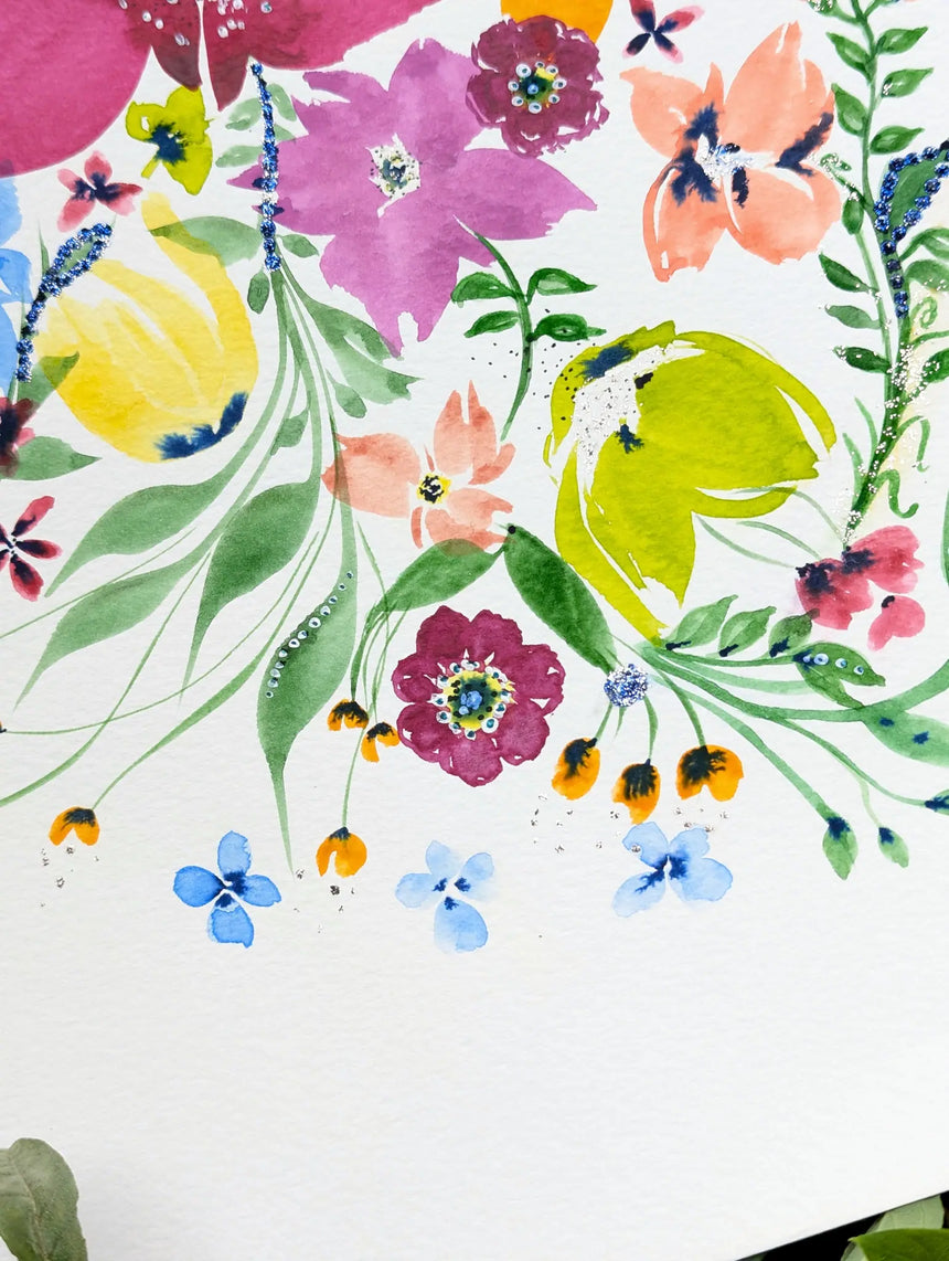 A close-up of a watercolor floral print on textured white paper, featuring vibrant flowers in pink, yellow, blue, orange and green with delicate leaves and stems.