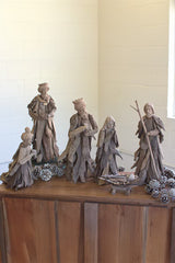 A rustic nativity scene carved from weathered driftwood, displayed on a wooden cabinet against a light-colored brick wall.