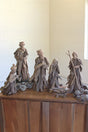 A rustic nativity scene carved from weathered driftwood, displayed on a wooden cabinet against a light-colored brick wall.