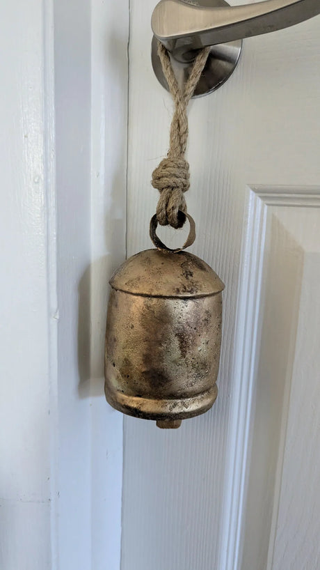Vintage-style metal bell with rope attached to a door handle on a white door.