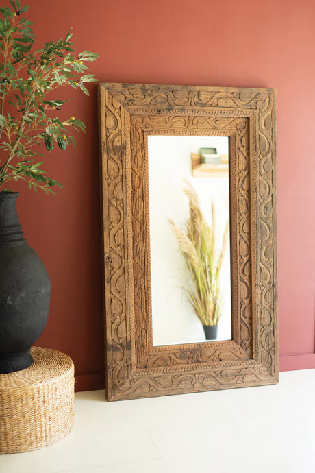 Decorative wooden frame with mirror on a wall next to a black vase and plant.