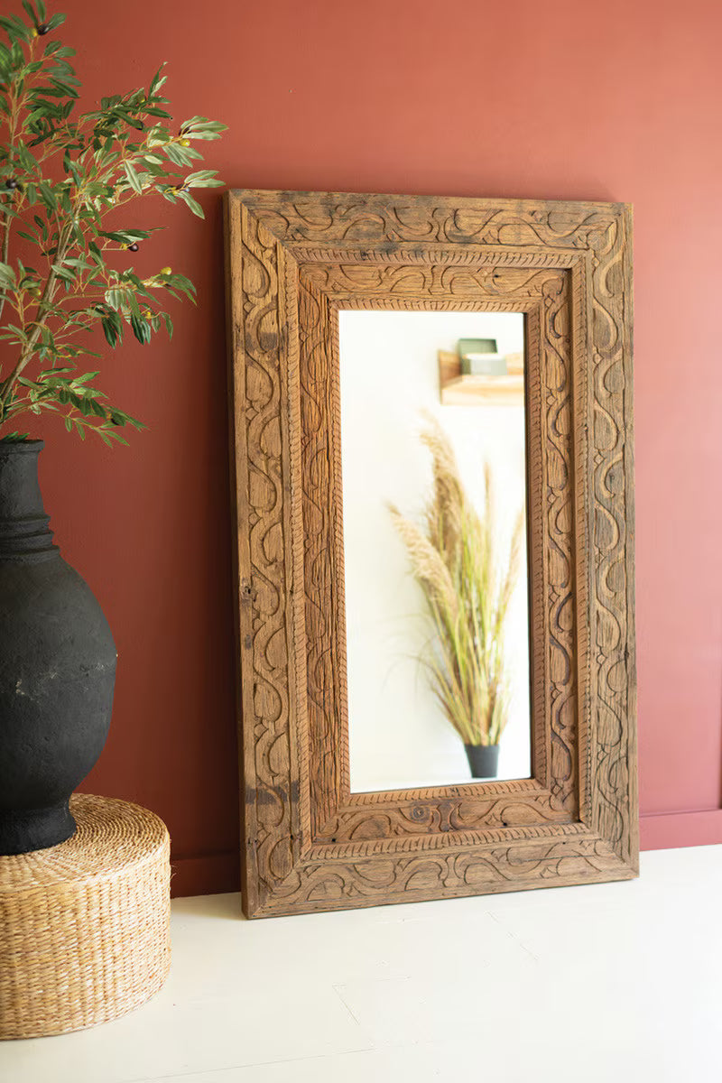 Decorative wooden frame with mirror on a wall next to a black vase and plant.