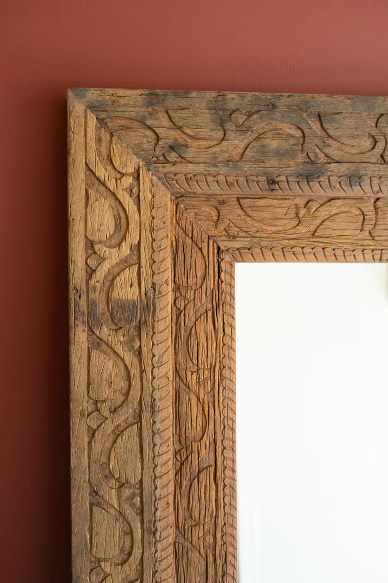 Wooden frame with intricate carvings hanging on a red-brown wall.