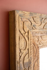 Close-up of a wooden frame with intricate carvings on a pink wall.