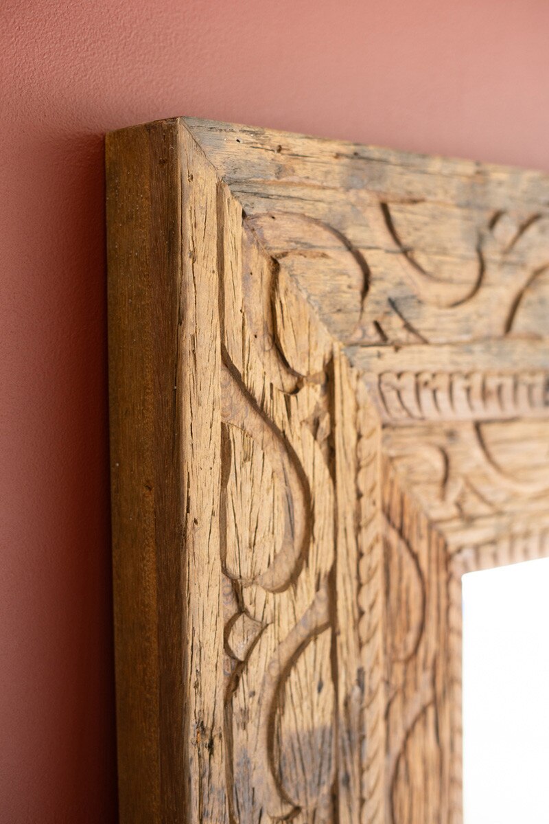 Close-up of a wooden frame with intricate carvings on a pink wall.