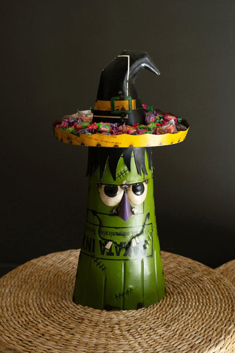 Halloween-themed candy holder with green face, black hat, and purple accents on a dark background.