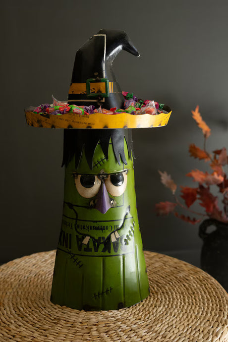 Halloween-themed decoration with a green witch figure and yellow hat on a dark background