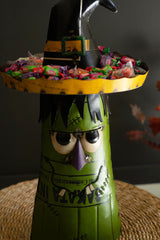 Halloween-themed candy holder with a witch design filled with colorful candies on a dark background.