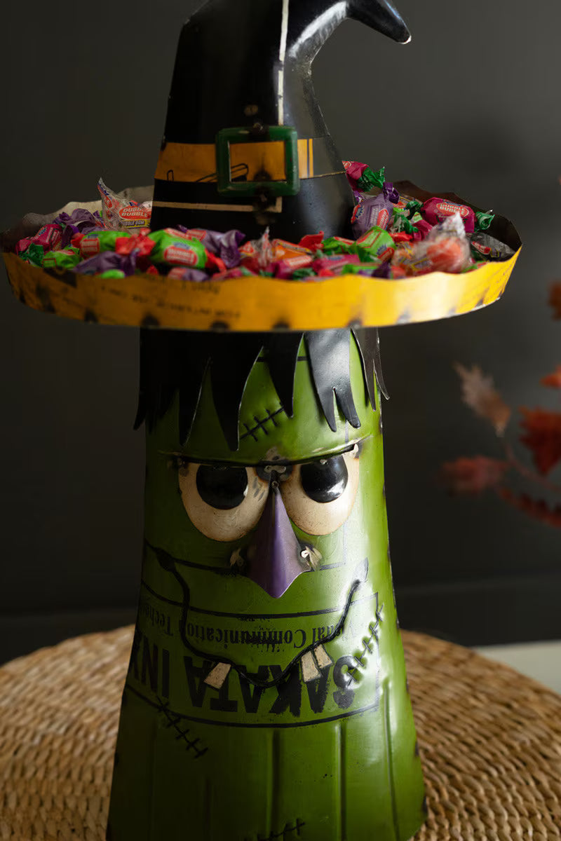 Halloween-themed candy holder with a witch design filled with colorful candies on a dark background.