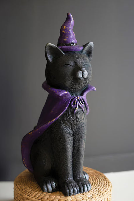Black cat figurine wearing a purple witch hat and cape on a gray background