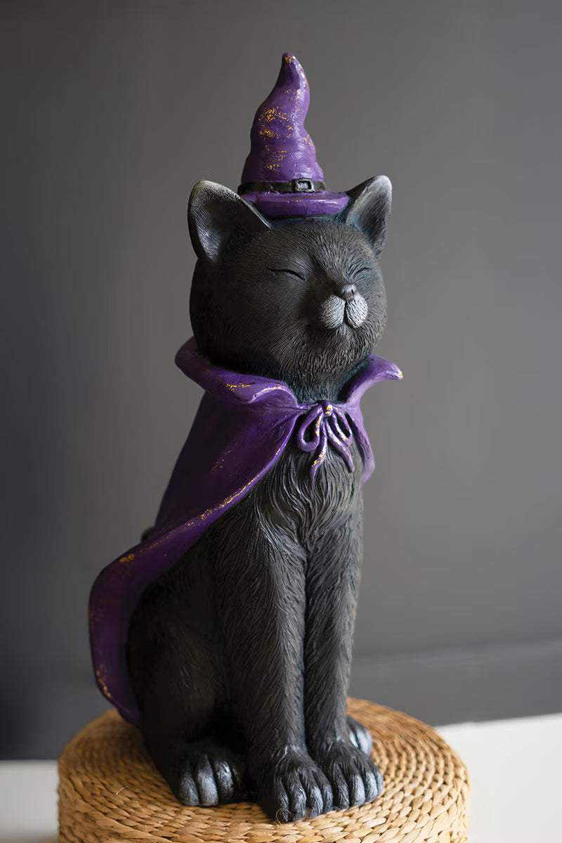 Black cat figurine wearing a purple witch hat and cape on a gray background