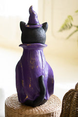 Purple cat-shaped bottle with a witch hat on a woven surface seen from the rear