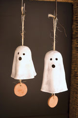 Two white clay ghost-shaped bells with brown tags on a dark background