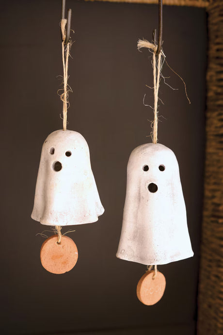 Two white clay ghost-shaped bells with brown tags on a dark background
