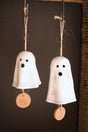 Two white clay ghost-shaped bells with brown tags on a dark background