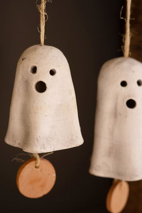 Two white clay ghost bells with brown tags on a dark background