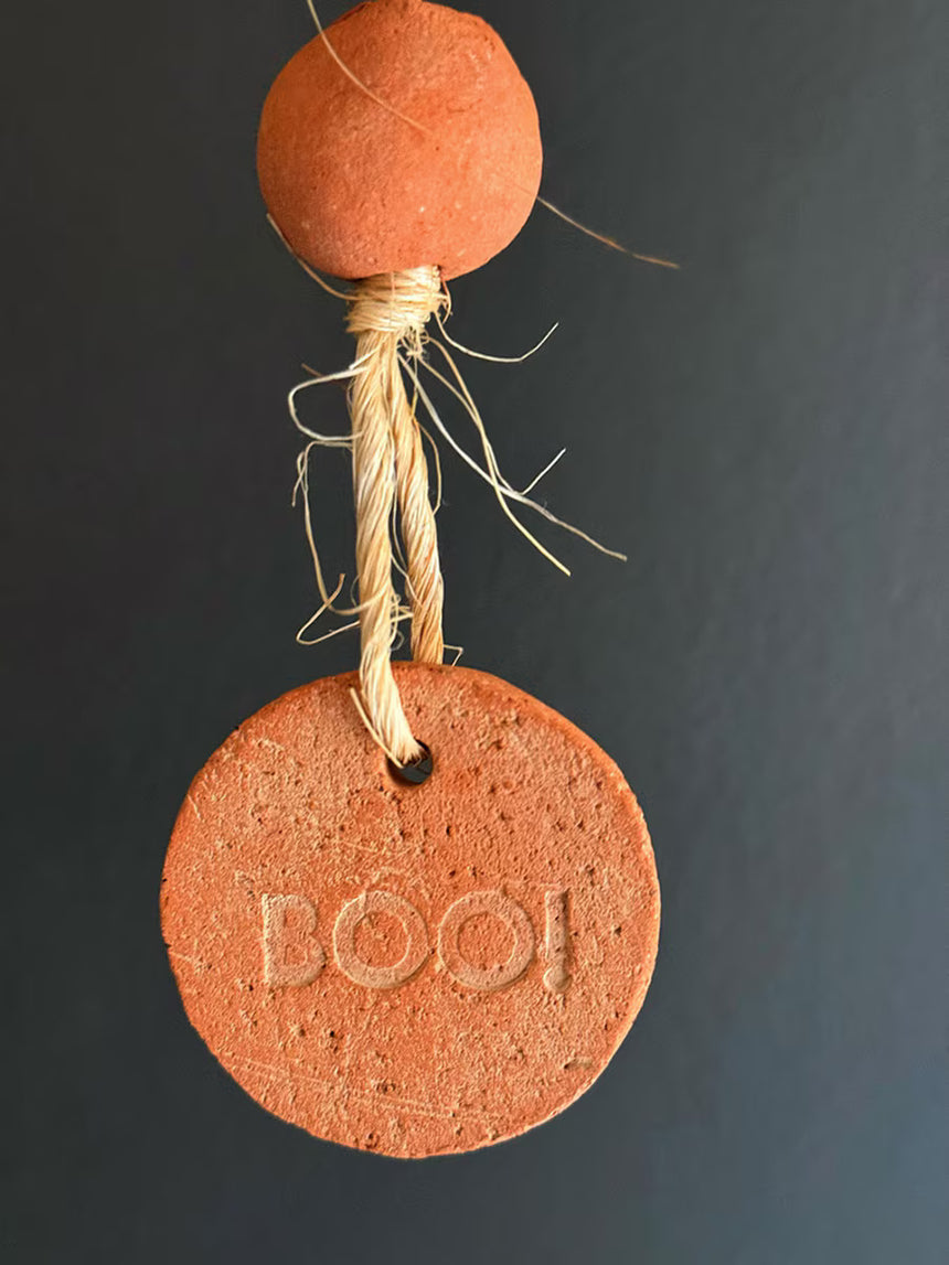 Terracotta-colored ornament with 'BOO!' text on a dark background