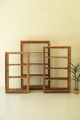 Three wooden shelves of different sizes against a beige wall with a plant on a white floor.