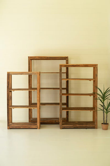 Three wooden shelves of different sizes against a beige wall with a plant on a white floor.