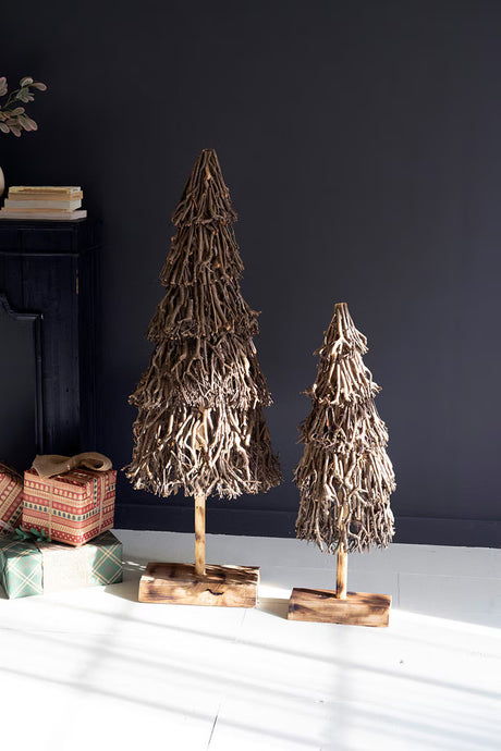 Two decorative twig trees on stands against a dark wall with gift boxes below.