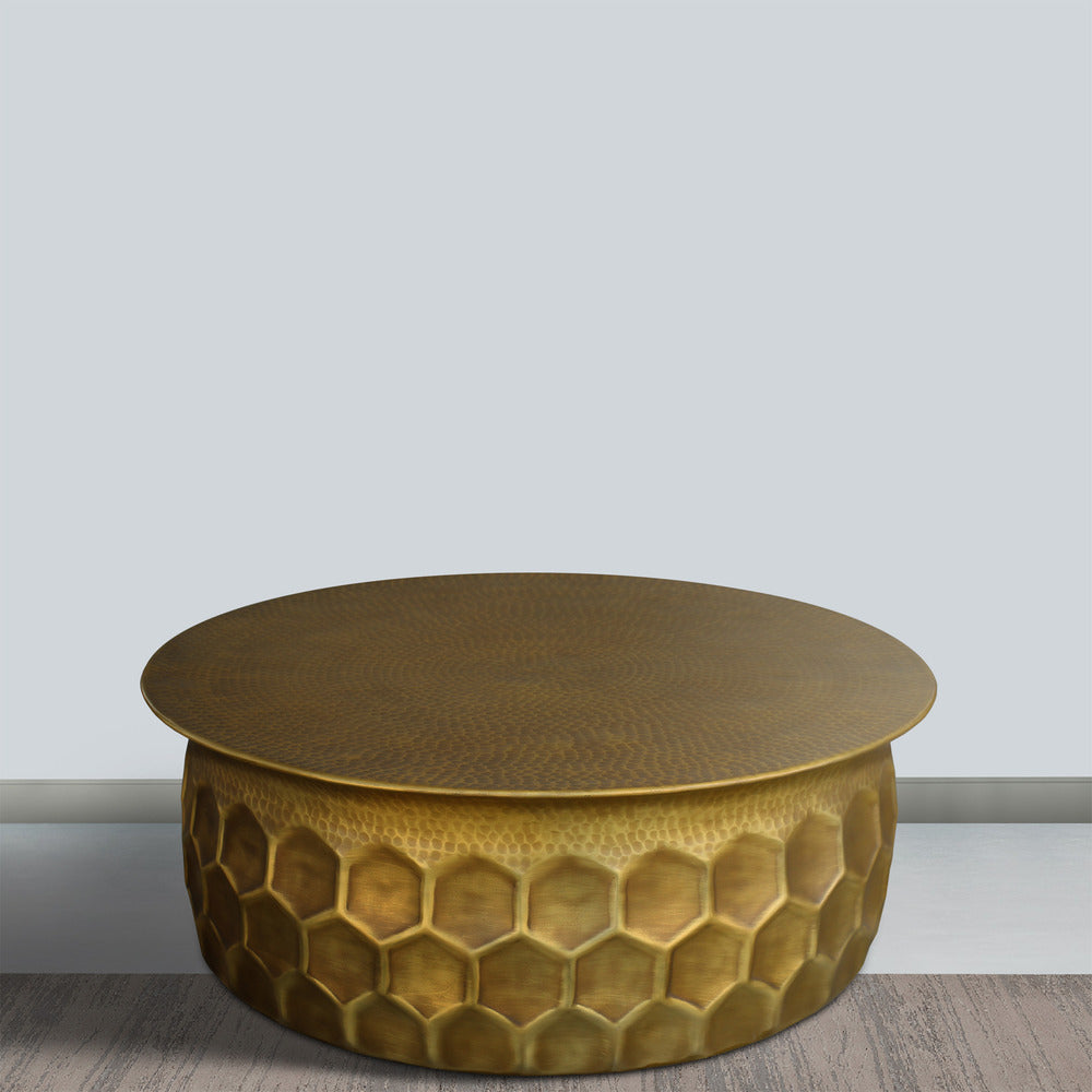 round hammered aluminum coffee table with brass finish on wood floor with white wall background