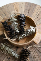 silver and dark brown metal pine cones laying in a wood bowl all resting on a rustic wood coffee table