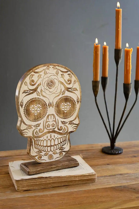 carved wood skull with calavera motif with burning candles in background - halloween decor