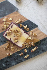 close up of honey covered cheese and nuts on christmas tree shaped wood and marble cutting board